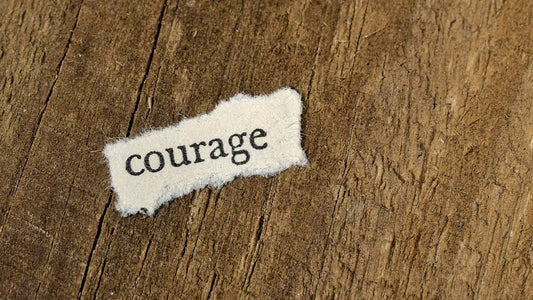 Tiny piece of paper on a wooden background that says Courage